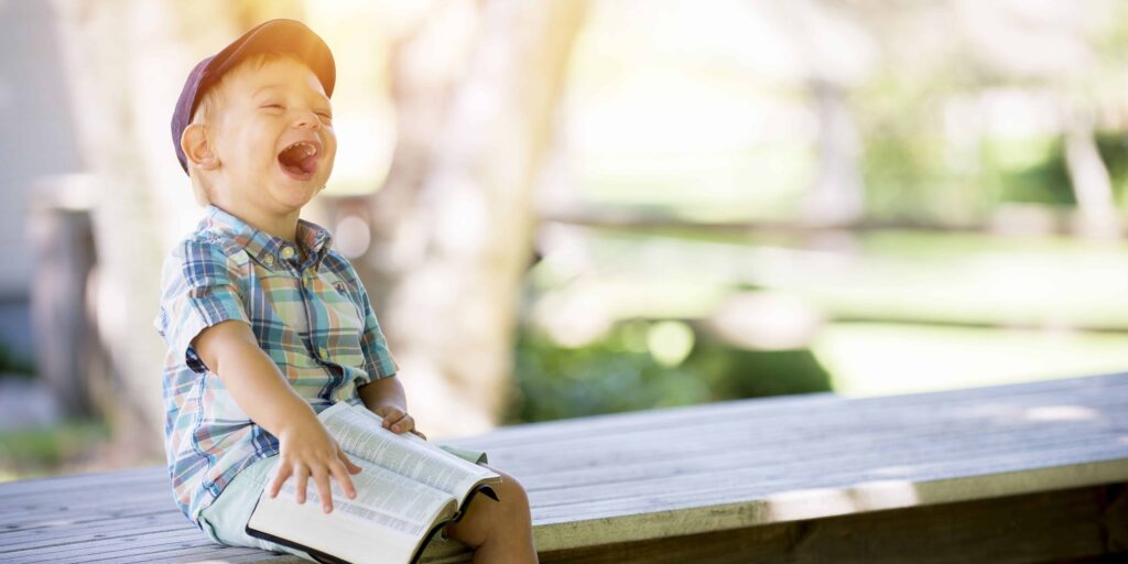 Billede af en lille dreng der sidder og griner med en bog